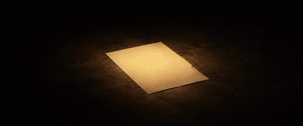 A single blank sheet of paper lying alone on dark ground, lit by one direct overhead light