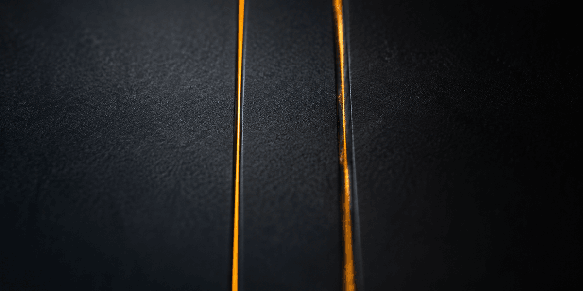 Two thin vertical lines of amber light cutting through a dark textured surface, one running clean and unbroken, the other dimming partway down, representing information that looks the same on the surface but only one version is actually read correctly underneath