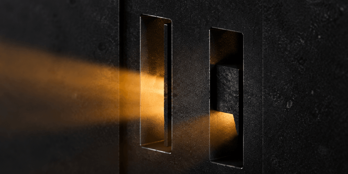 Two narrow openings in a dark textured wall lit by the same warm light — one projects a clear, directional beam outward, the other's light stays contained and diffuse just inside the opening