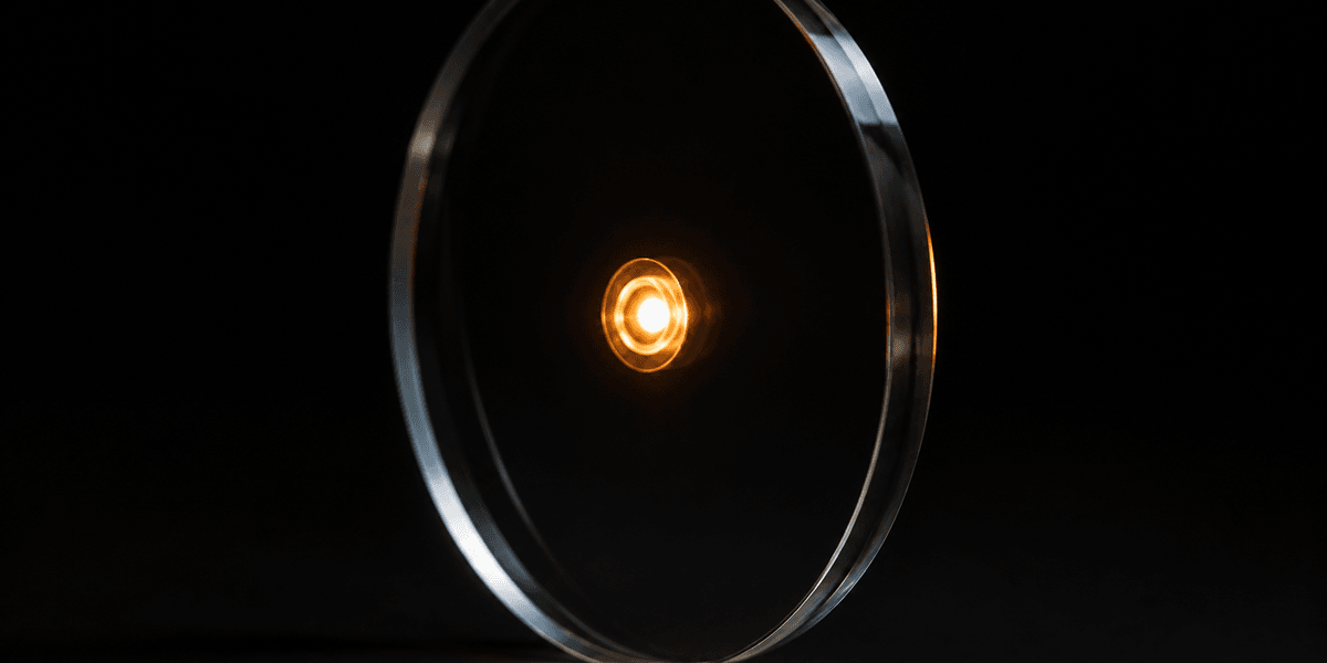 A warm light glowing fully visible at the center of a clear glass disk, nothing obscuring it from view, representing a price with nothing hidden behind it