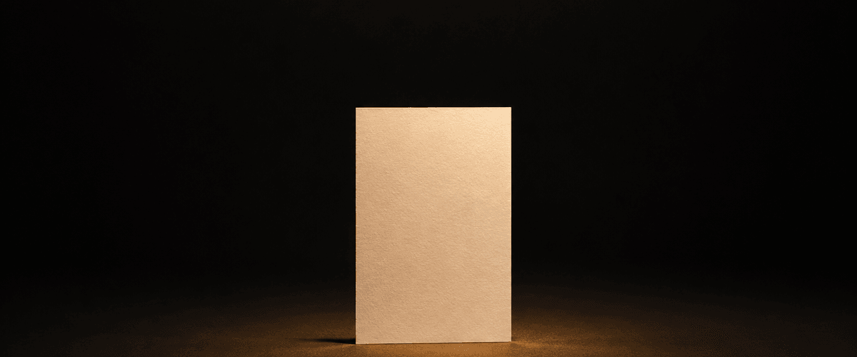 A single blank card standing upright under direct warm light in a dark space, representing a commitment laid out plainly enough for anyone to examine