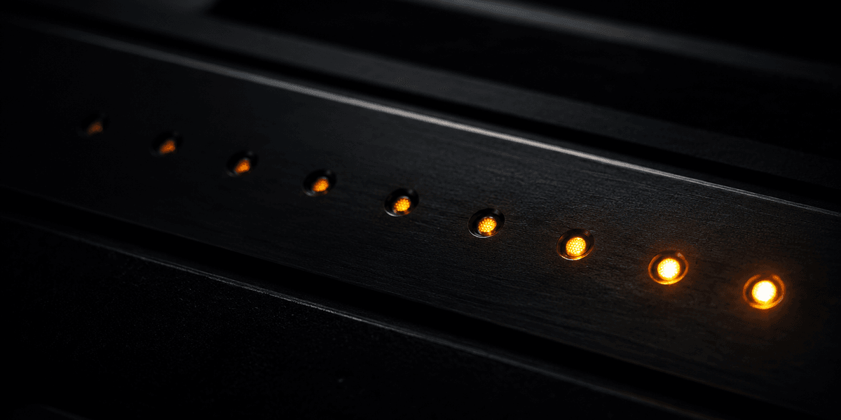 A close-up row of small lit points along a dark surface, dim at one end and glowing brighter at the other, representing how a series of small improvements builds gradually toward a much stronger result